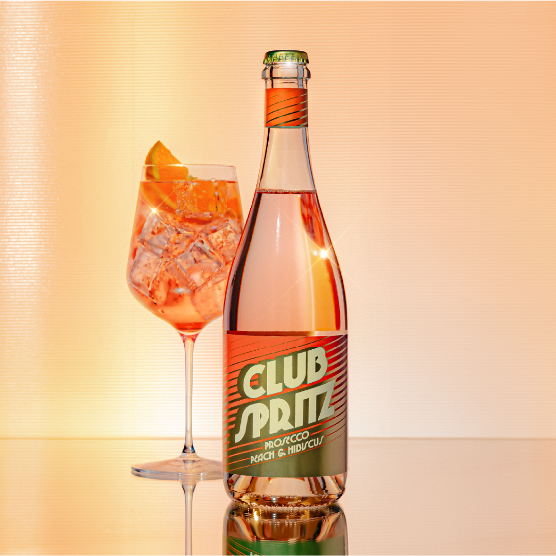 Stylised product shot of Club Spritz, Prosecco, Peach & Hibiscus spritz poured over ice and garnished with an orange slice.