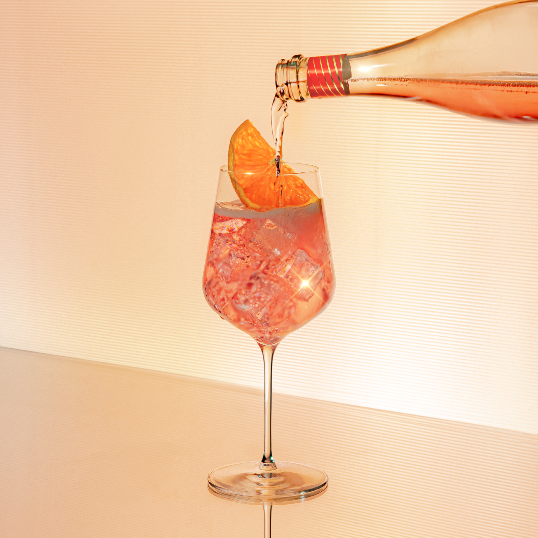 Prosecco, Peach & Hibiscus Spritz served over ice with a slice of orange.